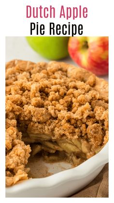 an apple pie with crumb topping in a white casserole dish next to apples