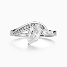 a white gold ring with two pear shaped diamonds on the band and an oval cut diamond in the center