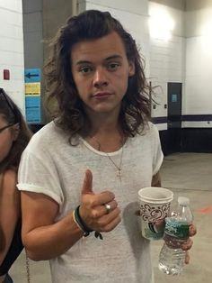 a man with long hair holding a cup and giving the thumbs up while standing next to a woman