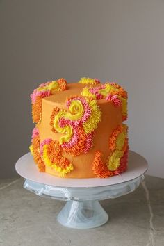 an orange and yellow cake with flowers on it sitting on a white plate in front of a gray wall