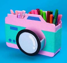 a pink and blue toy camera with pens, pencils, and markers in it