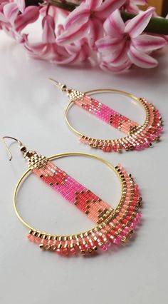 pink and gold beaded hoop earrings sitting on top of a table next to flowers