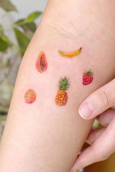 a person with fruit tattoos on their legs and one has a banana, oranges, and strawberries