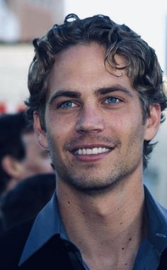 a close up of a person wearing a blue shirt and smiling at the camera with other people in the background