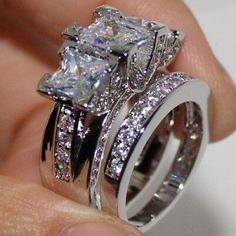 a person holding two wedding rings with diamonds on top of each one and the other hand