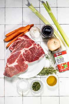 raw meat, vegetables and spices on a white tile counter top with utensils