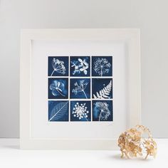 a white frame with blue flowers and leaves on it next to a vase filled with dried flowers