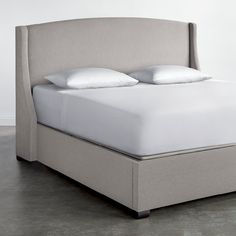 an upholstered bed with white pillows and linens on the headboard is shown