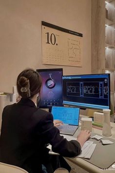 a woman sitting at a desk with two computer monitors and a laptop in front of her