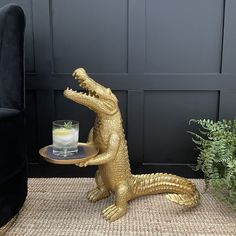 a gold alligator statue sitting on top of a table next to a chair and potted plant