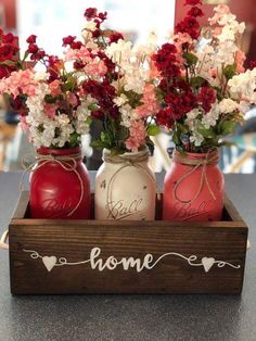 three mason jars with flowers in them are sitting on a counter top, and the word home is written across the jar