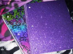 two notebooks with purple and green glitter covers on top of a zebra print blanket