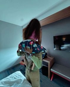 a woman holding a child in her arms while standing next to a bed and television