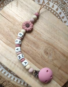 a pink pacifier necklace on a wooden board with words written in white and black