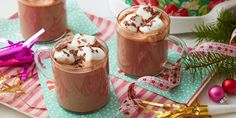 two glasses of hot chocolate with marshmallows on top and christmas decorations in the background