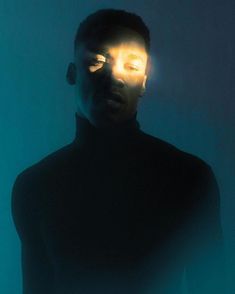 a man standing in front of a blue wall with the light shining through his eyes