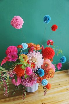 a vase filled with colorful flowers sitting on top of a wooden table next to a green wall