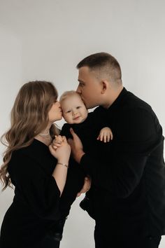 a man and woman holding a baby in their arms while they are kissing each other