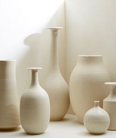 several white vases lined up against a wall