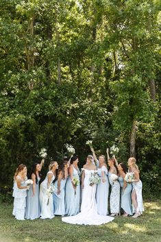 a group of bridesmaids posing for a photo in front of trees and grass