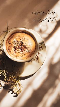 a cup of coffee on a saucer next to some dried flowers and arabic writing