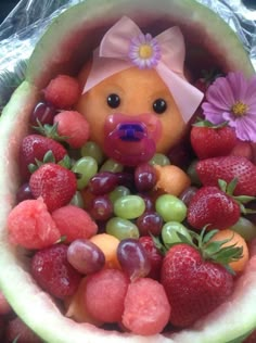 a teddy bear sitting inside of a watermelon bowl filled with grapes and strawberries