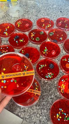 a hand is holding a red substance with colorful sprinkles on it in front of several clear bowls