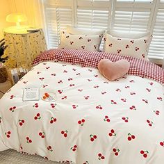 a white bed with cherries on it in a bedroom next to a lamp and window