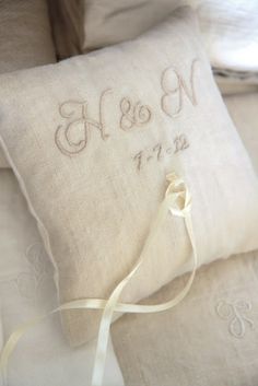 a white pillow that has the initials and date on it with a ribbon tied around it