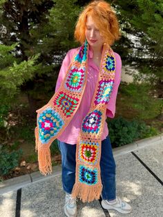 a woman with red hair wearing a pink shirt and colorful crocheted shawl