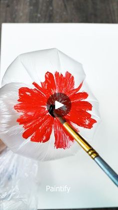 a person holding a paintbrush in front of a paper flower