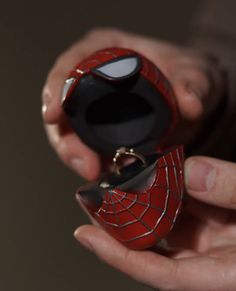 a person holding a ring with a spiderman face on it's cover in their hands