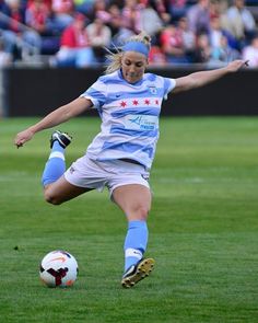 a woman kicking a soccer ball on top of a field