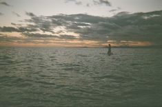 a person on a surfboard in the ocean at sunset with clouds and water behind them