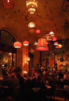 people sitting at tables in a restaurant with lights hanging from the ceiling