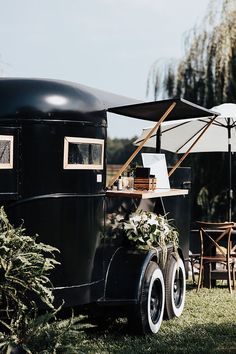 an old fashioned food truck is parked in the grass with an umbrella over it's head