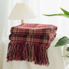 two blankets are stacked on top of each other next to a lamp and potted plant