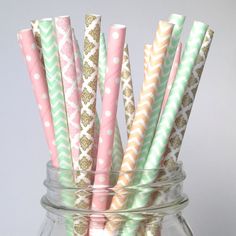 several pink and green paper straws in a glass jar with gold glitter on top