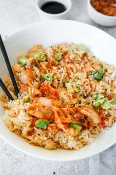 a white bowl filled with rice and vegetables next to chopsticks on the side