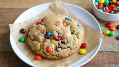 a chocolate chip cookie with m & m candies on it next to a bowl of candy