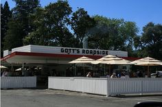 people are sitting at tables under umbrellas in front of a food stand that is white and red