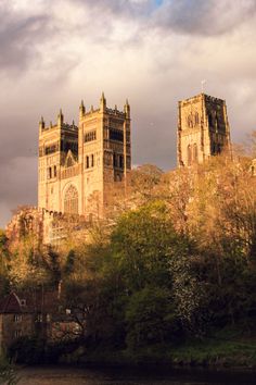 an old castle with two towers on the top and trees around it, against a cloudy sky