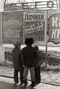 three young boys are standing in front of a sign that reads russian and has advertisements on it