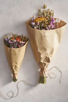 two bouquets of flowers wrapped in brown paper on a white surface with twine