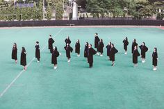 a group of people in graduation gowns standing on a tennis court with trees in the background