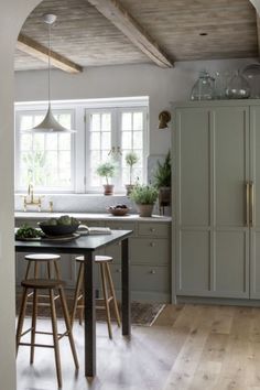 a kitchen with wooden floors and white walls, an island in the middle is surrounded by stools