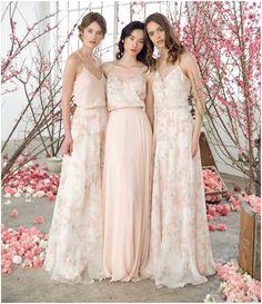 three women standing next to each other in long dresses with pink flowers on the ground