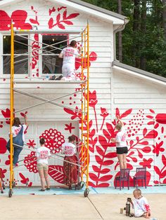 people are painting the outside of a house with red leaves on it and white walls