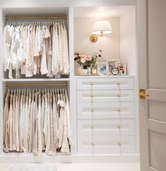 an open closet with clothes hanging on the wall, and a lamp next to it