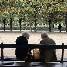 two elderly people sitting on a bench in a park, one holding a bag and the other looking at something